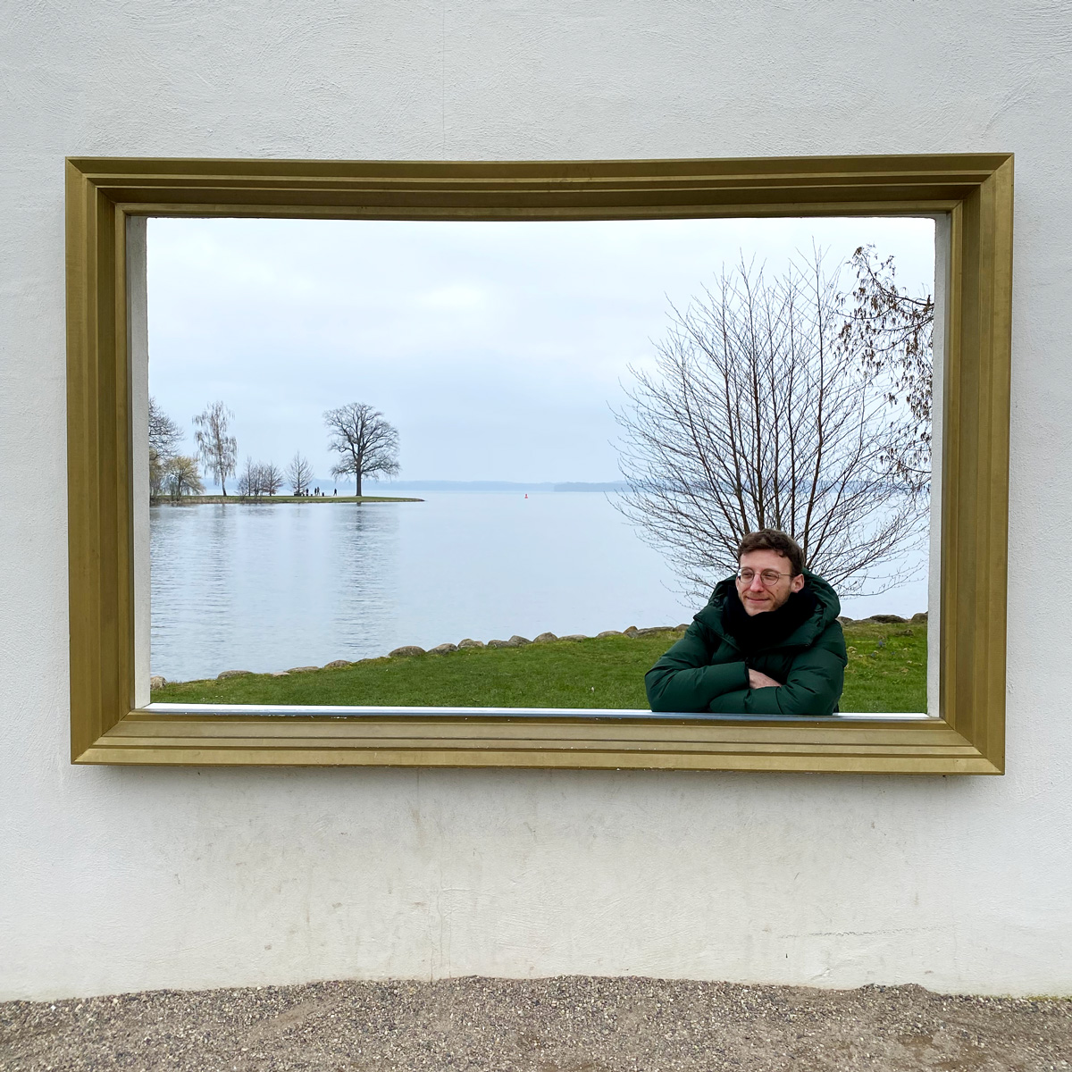 Me sitting in a big golden picture frame outside, in the back of the picture: a lake and tree