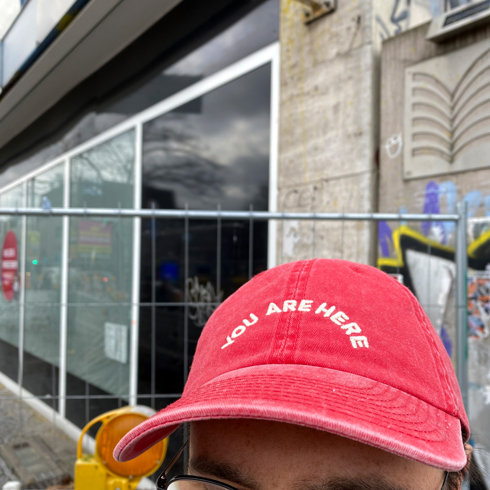 Photo of a person wearing a red hat which says “You are here”