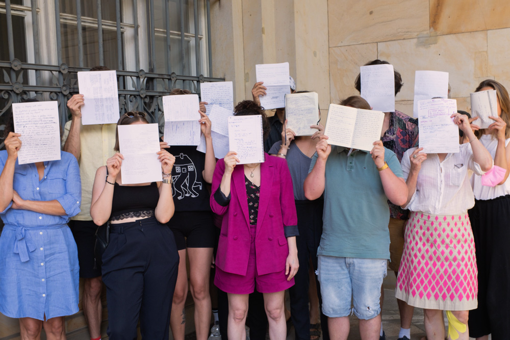 Team photo of a previous Writing class; people holding their manuscripts in front of their faces